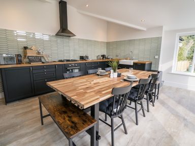 A kitchen with a wooden dining table and black chairs next to black cabinets and a tiled backsplash at Cooper's Rest in Dolwyddelan