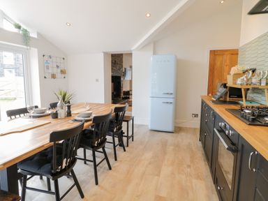 A kitchen and dining area with a wooden table set with dishes and chairs a light blue refrigerator and black cabinets at Cooper's Rest Gorffwysfa Coopers in Dolwyddelan
