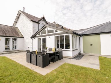 An outdoor patio area with a black dining table and chairs next to a white house with a green door at Cooper's Rest Gorffwysfa Coopers in Dolwyddelan