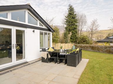 An outdoor patio area with black wicker furniture and a glass table next to a white building at Coopers Rest Gorffwysfa Coopers in Dolwyddelan