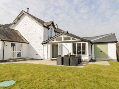 A house with white exterior walls a patio with outdoor dining furniture and a green lawn at Cooper's Rest Gorffwysfa Coopers in Dolwyddelan