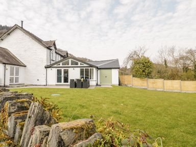 A backyard with a green lawn patio dining set and a white house with a stone wall and wooden fence at Cooper's Rest Gorffwysfa Coopers in Dolwyddelan