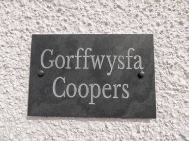 A black plaque with the text Gorffwysfa Coopers mounted on a white textured wall at Coopers Rest Gorffwysfa Coopers in Dolwyddelan