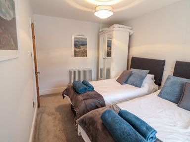 A bedroom with two single beds with blue and gray pillows and blue rolled towels at Cooper's Rest in Dolwyddelan