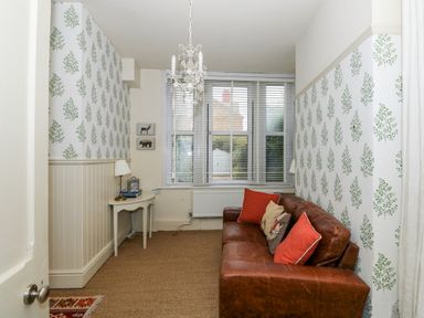 A small room with a brown leather sofa and patterned wallpaper at Troon Cottage in Hunstanton