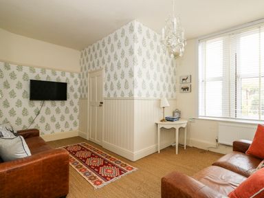 A living room with two brown leather sofas a wall-mounted TV a patterned rug and a small table with a lamp at Troon Cottage in Hunstanton