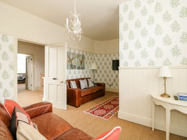 A living room with two leather sofas a side table with a lamp and patterned wallpaper at Troon Cottage in Hunstanton