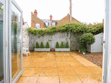 A garden with tiled flooring a white lattice fence potted plants and a shed at Troon Cottage in Hunstanton
