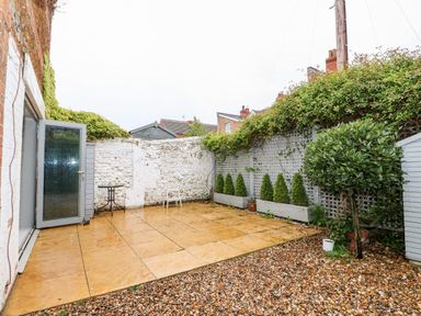 A small backyard with a tiled patio gravel area potted plants and a white brick wall at Troon Cottage in Hunstanton
