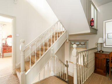 A staircase with white balusters and beige carpet near a wooden desk and mirror at Troon Cottage in Hunstanton