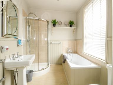 A bathroom with a sink, a glass shower enclosure, a bathtub, and a window with blinds at Troon Cottage in Hunstanton