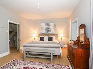 A bedroom with a bed and bench at the foot of the bed two bedside tables with lamps a wooden dresser with mirror and a patterned rug on the floor at Troon Cottage in Hunstanton