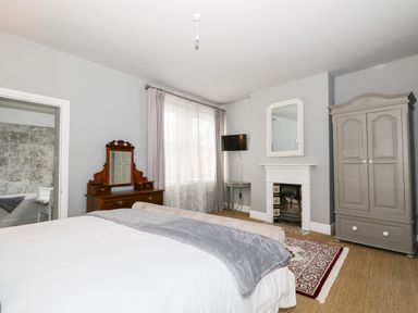 A bedroom with a bed a wooden dresser a wardrobe a small TV and a fireplace at Troon Cottage in Hunstanton