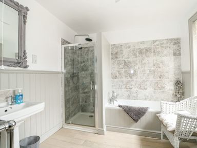 A bathroom with a shower enclosure bathtub with a towel wicker chair sink with soap and mirror at Troon Cottage Hunstanton