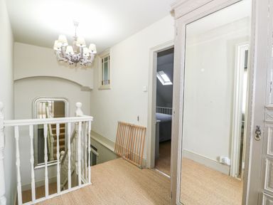 A hallway with a carpeted floor a chandelier a mirror a wooden gate and a doorway leading to a bedroom at Troon Cottage in Hunstanton