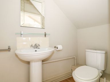 A bathroom with a pedestal sink a mirror a toilet and a toilet paper holder at Troon Cottage in Hunstanton
