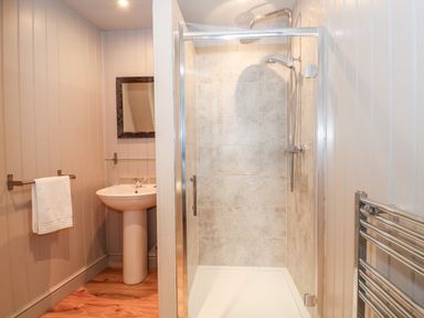 A bathroom with a shower cubicle a pedestal sink a towel rail and wooden flooring at Troon Cottage in Hunstanton