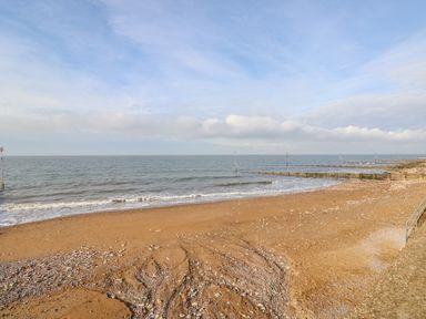 A sandy beach with small waves and wooden groynes extending into the sea at Troon Cottage in Hunstanton