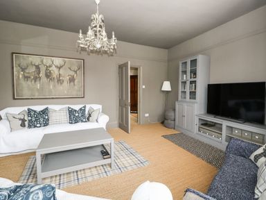 A living room with sofas cushions a coffee table a TV cabinet and a chandelier at Troon Cottage in Hunstanton