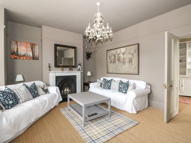 A living room with a fireplace two white sofas a gray coffee table and wall art at Troon Cottage in Hunstanton