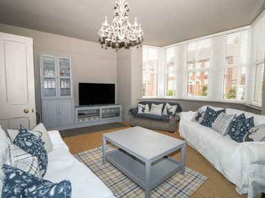 A living room with a chandelier two sofas a coffee table and a TV unit at Troon Cottage in Hunstanton