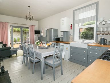 A kitchen dining area with gray chairs around a table a refrigerator a sink and a window at Troon Cottage in Hunstanton