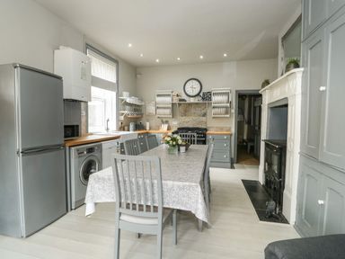 A kitchen with a dining table and chairs fridge washing machine and a fireplace at Troon Cottage in Hunstanton