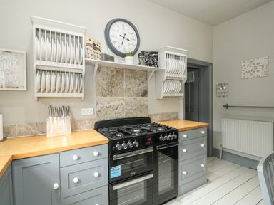 A kitchen with gray cabinets a black oven a gas stove wooden countertops and plates on wall racks at Troon Cottage in Hunstanton