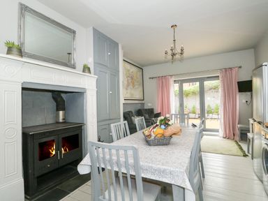 A dining room with a fireplace table with chairs and sliding glass doors with pink curtains at Troon Cottage in Hunstanton