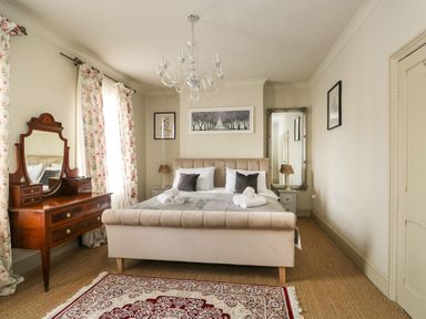 A bedroom with a bed a dressing table a chandelier and a rug at Troon Cottage in Hunstanton