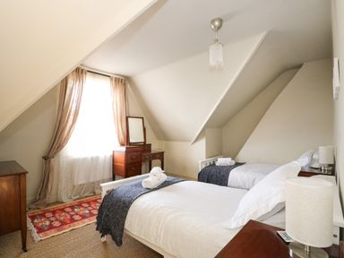 A bedroom with two single beds bedside tables a dresser with a mirror and a window with curtains at Troon Cottage in Hunstanton