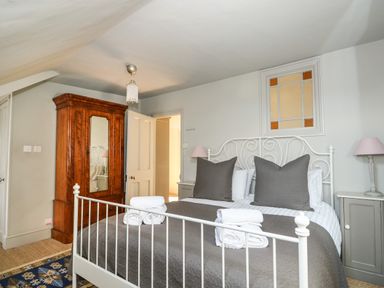 A bedroom with a white metal bed frame grey bedding two bedside tables and a wooden wardrobe at Troon Cottage in Hunstanton