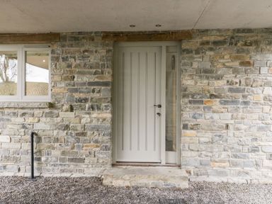 A stone exterior wall with a light gray door and adjacent window at Willow Barn in Shapwick