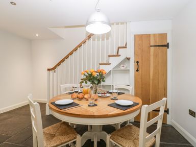 A dining area with a round wooden table and four chairs with woven seats near stairs and a wooden door at Willow Barn in Shapwick