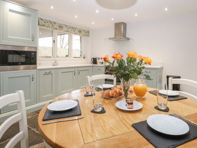A kitchen with a round wooden dining table set for four with plates glasses and cutlery at Willow Barn in Shapwick