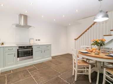 A kitchen with green cabinets a stainless steel oven a round dining table with chairs and a staircase in the background at Willow Barn in Shapwick
