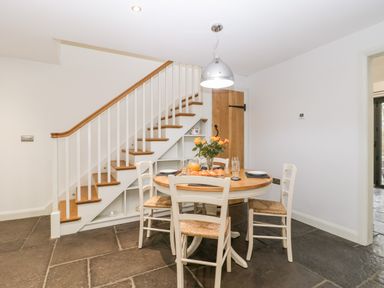 A dining area with a round wooden table set with plates and glasses beside a wooden staircase at Willow Barn in Shapwick