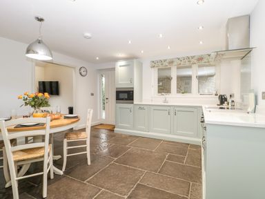 A kitchen with light green cabinets a round dining table with chairs and a hanging light at Willow Barn in Shapwick