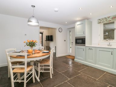 A kitchen with a round wooden dining table and four chairs with a vase of flowers and croissants on the table at Willow Barn in Shapwick