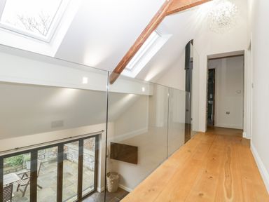 A hallway with wooden floor and glass railing overlooking a patio with table and chairs at Willow Barn in Shapwick