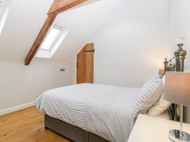 A bedroom with a double bed a bedside table with a lamp a skylight window exposed wooden beam and a wooden door at Willow Barn in Shapwick