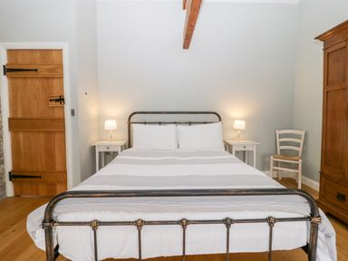 A bedroom with a bed in the center flanked by two nightstands with lamps a wooden door a chair and a wooden wardrobe at Willow Barn in Shapwick