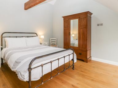 A bedroom with a double bed bedside tables a wooden chair and a wooden wardrobe with a mirror at Willow Barn in Shapwick