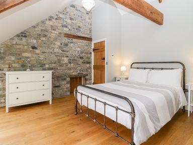 A bedroom with a metal bed frame bedside tables with lamps a white dresser and a stone wall at Willow Barn in Shapwick