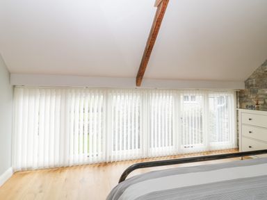 A bedroom with a bed frame near a large window with vertical blinds and a dresser at Willow Barn in Shapwick