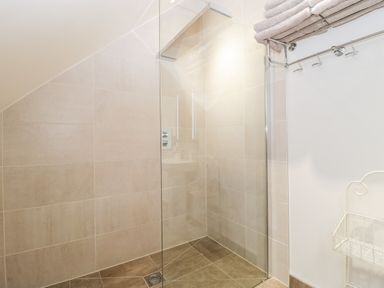 A tiled walk in shower area with a glass screen towels on a rack and a wire basket at Willow Barn in Shapwick