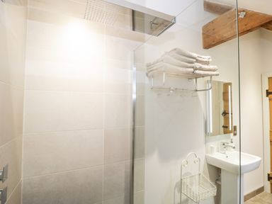 A bathroom with a tiled shower area towels on a rack a sink with a mirror and wooden door beams at Willow Barn in Shapwick