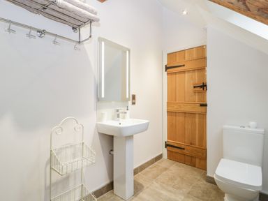 A bathroom with a wooden door a white sink a toilet a towel rack and a metal basket stand at Willow Barn in Shapwick