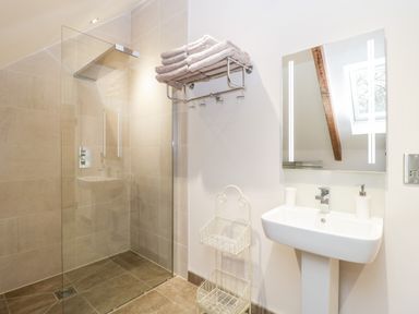 A bathroom with a walk-in shower a towel rack a sink with a mirror and a small storage rack at Willow Barn in Shapwick