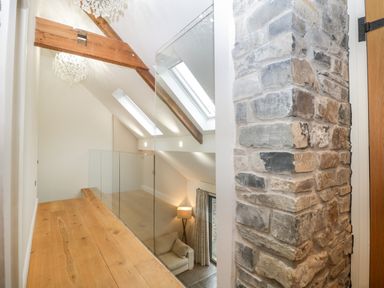 An upstairs hallway with wooden beams glass railing and a stone wall at Willow Barn in Shapwick
